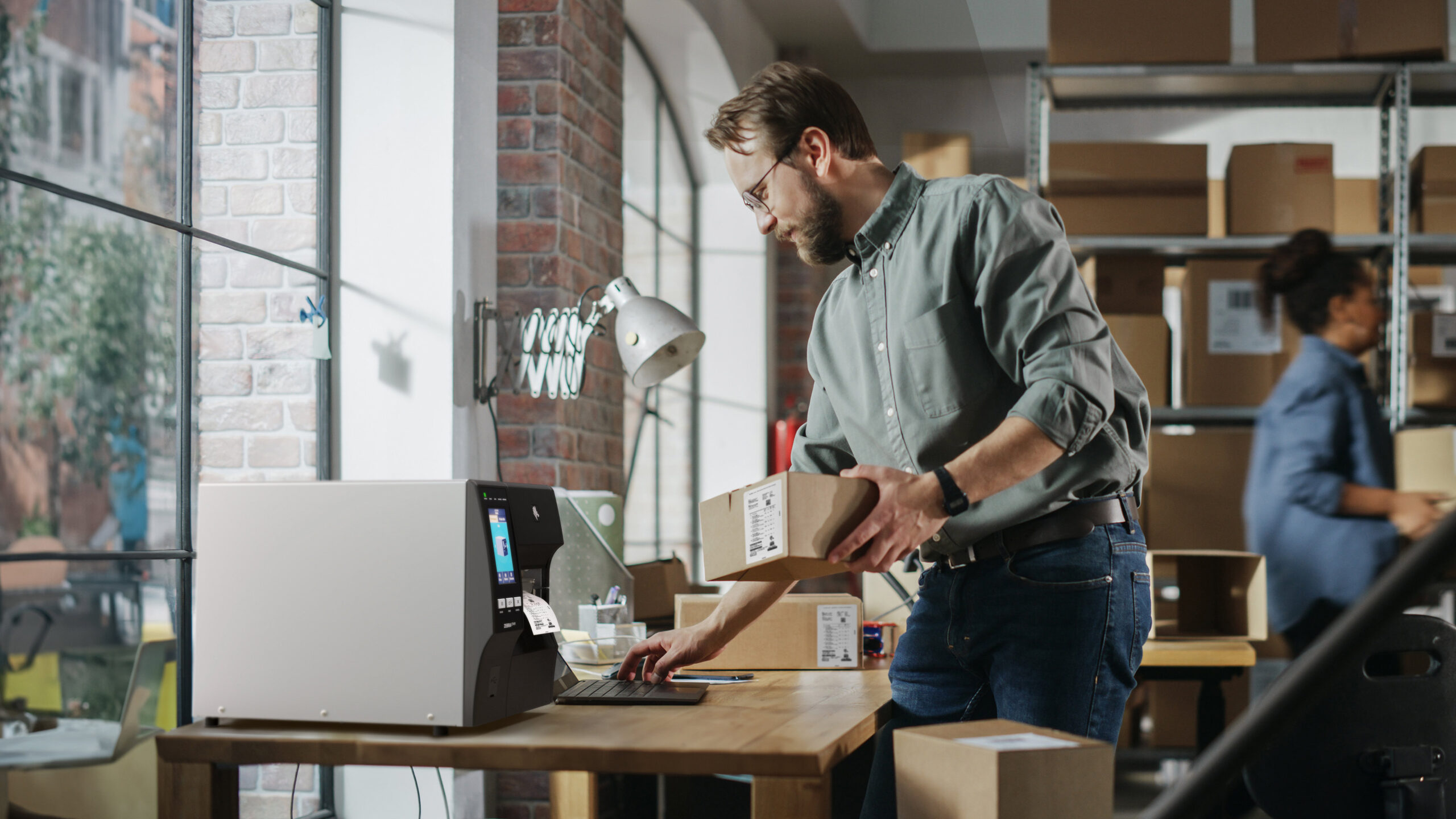 Απεικονίζεται ένας άνδρας ο οποίος κρατά ένα δέμα και εκτυπώνει ετικέτα από έναν θερμικό εκτυπωτή.